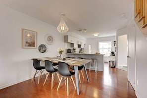 A modern kitchen with a dining area, wooden flooring, and a pendant light. - La Place du Village (Magog)