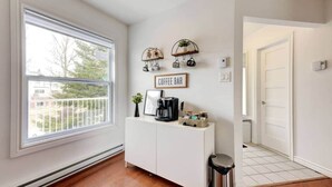 A room with a large window, a white console table with a coffee maker, and a 'Coffee Bar' sign. - La Place du Village (Magog)