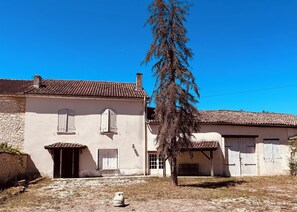 Ein traditionelles Gebäude mit Ziegeldach, Steinmauer und einem großen Baum davor.