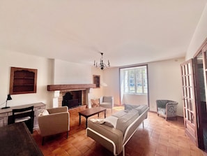 A living room with a fireplace, a sofa, a dining table, and a lamp. - Country house near Angoulême, 4 bedrooms (Torsac)