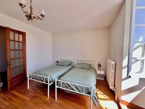 Een slaapkamer met twee bedden, een houten vloer, een radiator en een raam.