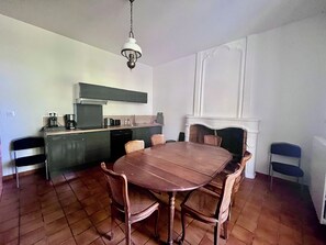 Een eetgedeelte met een houten tafel en stoelen, een keuken met moderne apparatuur, en een witte open haard.