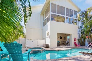 Una casa de dos pisos con piscina, mobiliario exterior y patio trasero cercado.