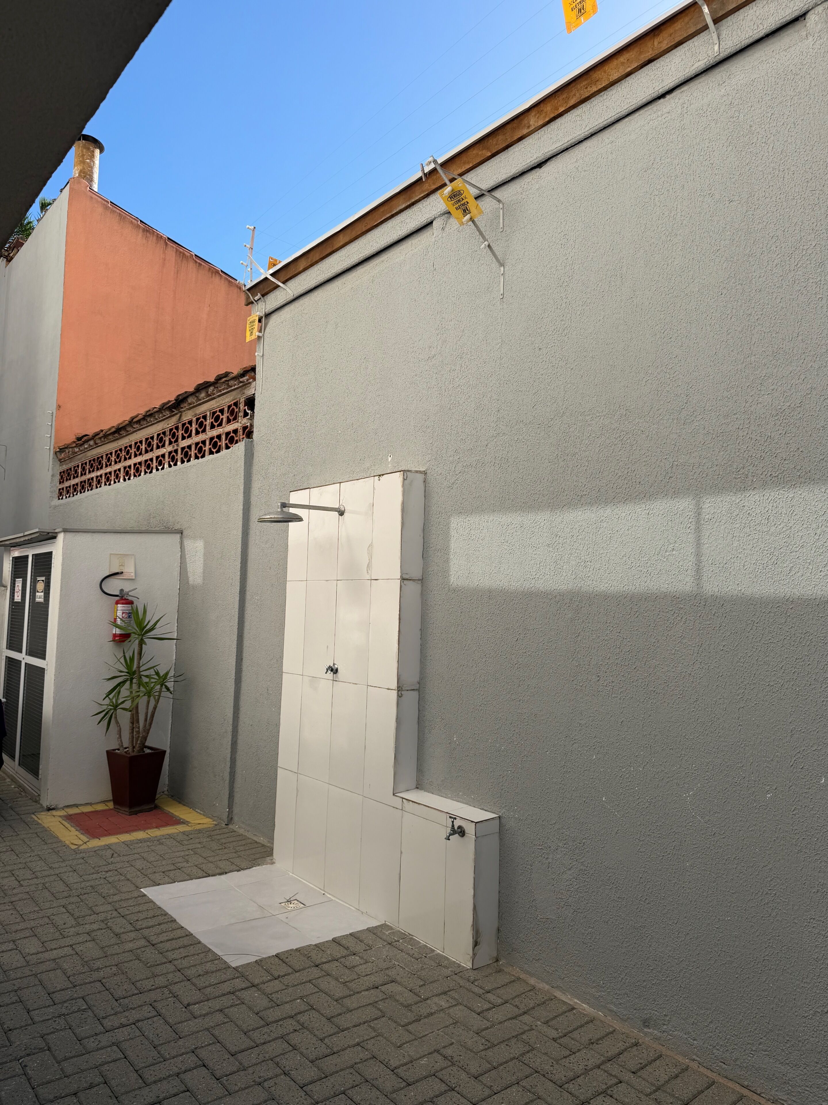 Exterior d'un edifici amb una paret gris, un extintor, una planta en test i una porta blanca.