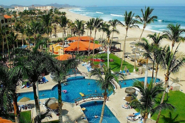 Resort com área de piscina, palmeiras e vista para a praia.