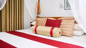 A bed with a red and white striped bedspread, a beige pillow with a red band, and a wooden headboard. - Habarana Inn - Offiacl (Habarana)