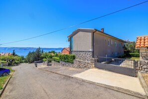 En bostadsgata med ett hus som har en fasad av sten, en uppfart med grind och utsikt över havet.