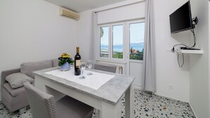 A modern room with a dining table, a sofa, a TV mounted on the wall, and a window with a view. - Cozy apartment for 2 people in Novi Vinodolski with balcony and barbecue (Novi Vinodolski)