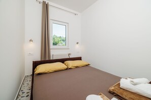 A bedroom with a bed, two pillows, a window, a radiator, and a towel on a wooden tray. - Cozy apartment for 2 people in Novi Vinodolski with balcony and barbecue (Novi Vinodolski)