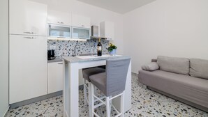 A compact kitchenette with a countertop, a chair, a sofa, and a potted plant. - Cozy apartment for 2 people in Novi Vinodolski with balcony and barbecue (Novi Vinodolski)