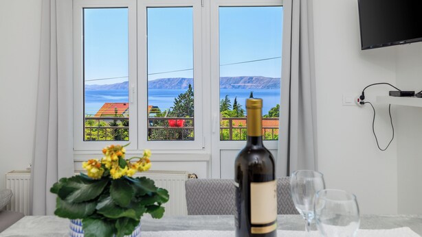 A room with a large window, a bottle of wine, and two glasses on a table. - Cozy apartment for 2 people in Novi Vinodolski with balcony and barbecue (Novi Vinodolski)