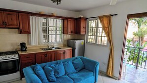 Une cuisine avec des meubles de rangement en bois, un réfrigérateur, une cuisinière et un canapé bleu.