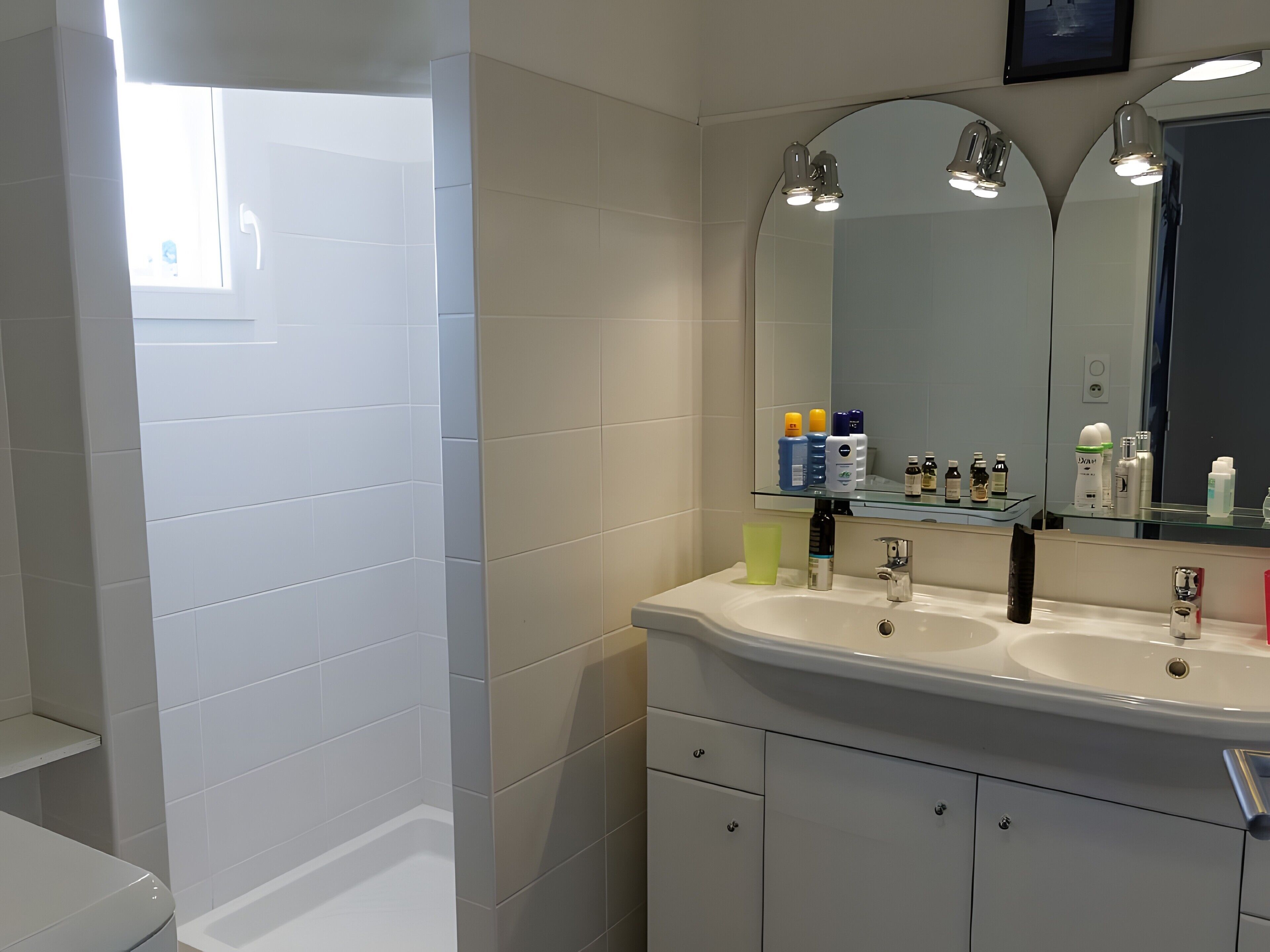 Un bagno moderno con piastrelle bianche, uno specchio grande, due lavabi e diversi articoli da toilette sul ripiano.