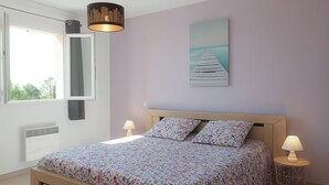 Un dormitorio con cama, dos lámparas de noche, una ventana con cortinas, un calentador de pared y un cuadro de un muelle.