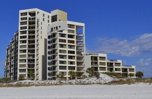 Hotel com vários andares e varandas, situado numa praia de areia.
