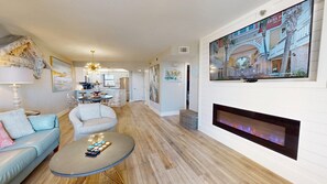 Un salon moderne avec une cheminée, un coin repas et une cuisine en arrière-plan.