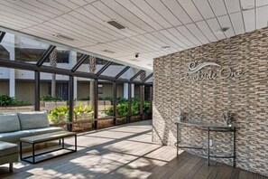 Uma área de pátio interna moderna com um compartimento de vidro, uma parede de pedra com a inscrição 'Beachside One', um sofá e uma pequena mesa.