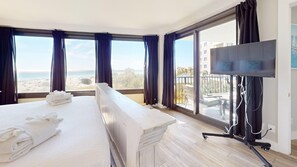 Ein Hotelzimmer mit einem Bett, einem Fernseher und großen Fenstern mit Vorhängen.