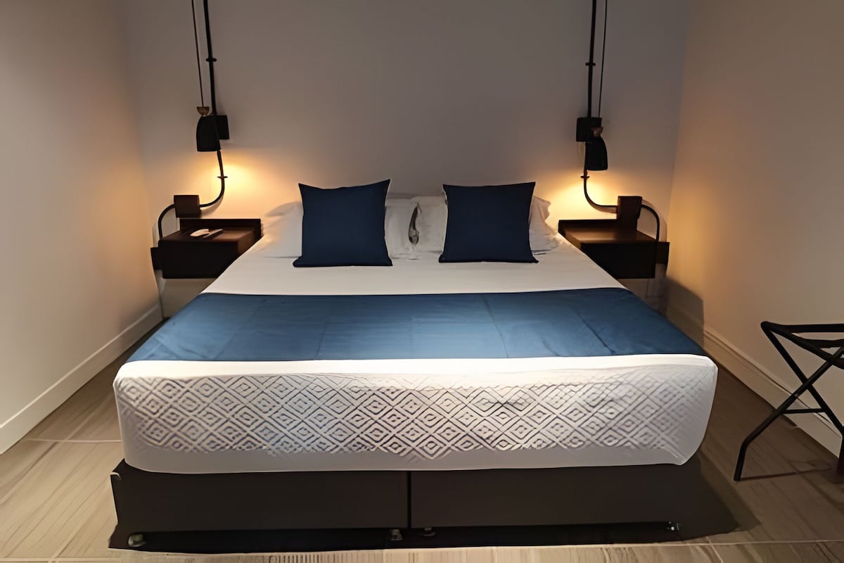 Una cama bien hecha con una colcha estampada, dos almohadas y dos mesitas de noche con lámparas.