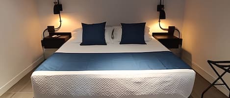 Una cama bien hecha con una colcha estampada, dos almohadas y dos mesitas de noche con lámparas.