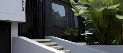 A modern building with a staircase leading to a door, a large green plant, and a tiled floor.