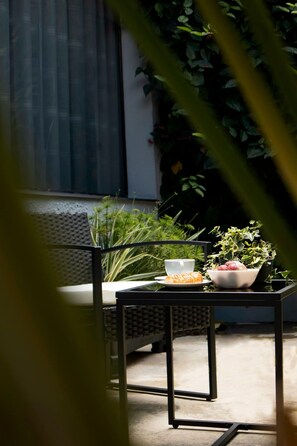Una mesa con un bol de fruta y una taza, en un balcón con vistas a zonas verdes y un edificio al fondo.