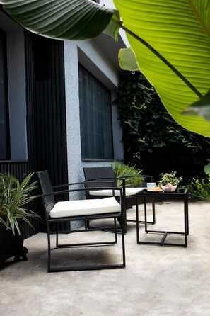 An outdoor seating area with two chairs and a table, surrounded by potted plants and a building with a dark facade. - Bluelux MDE B&B (Medellín)