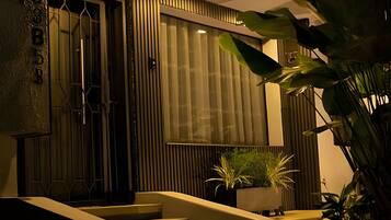 A staircase leading to a door with a number plate, a window with blinds, and potted plants.