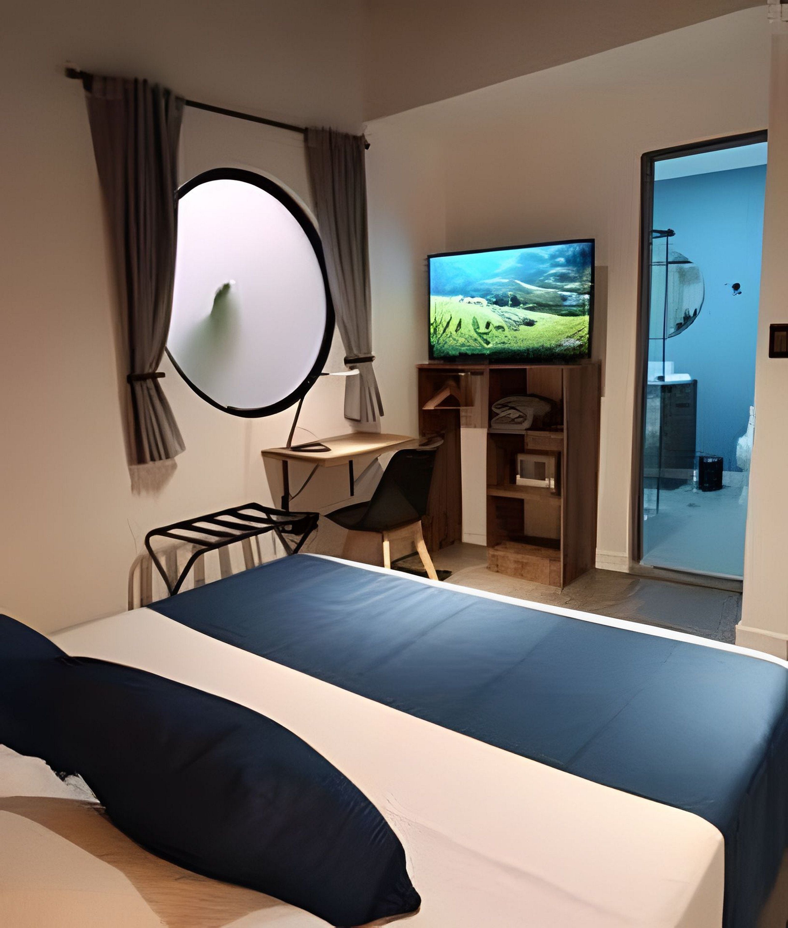 A hotel room with a bed, a desk, a chair, a television, and a wardrobe.