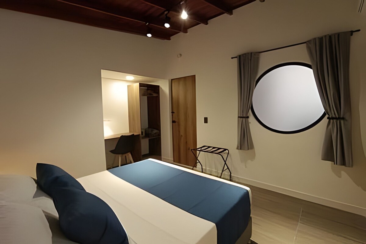 A bedroom with a bed, a wardrobe, a mirror, a round window, and a small table.