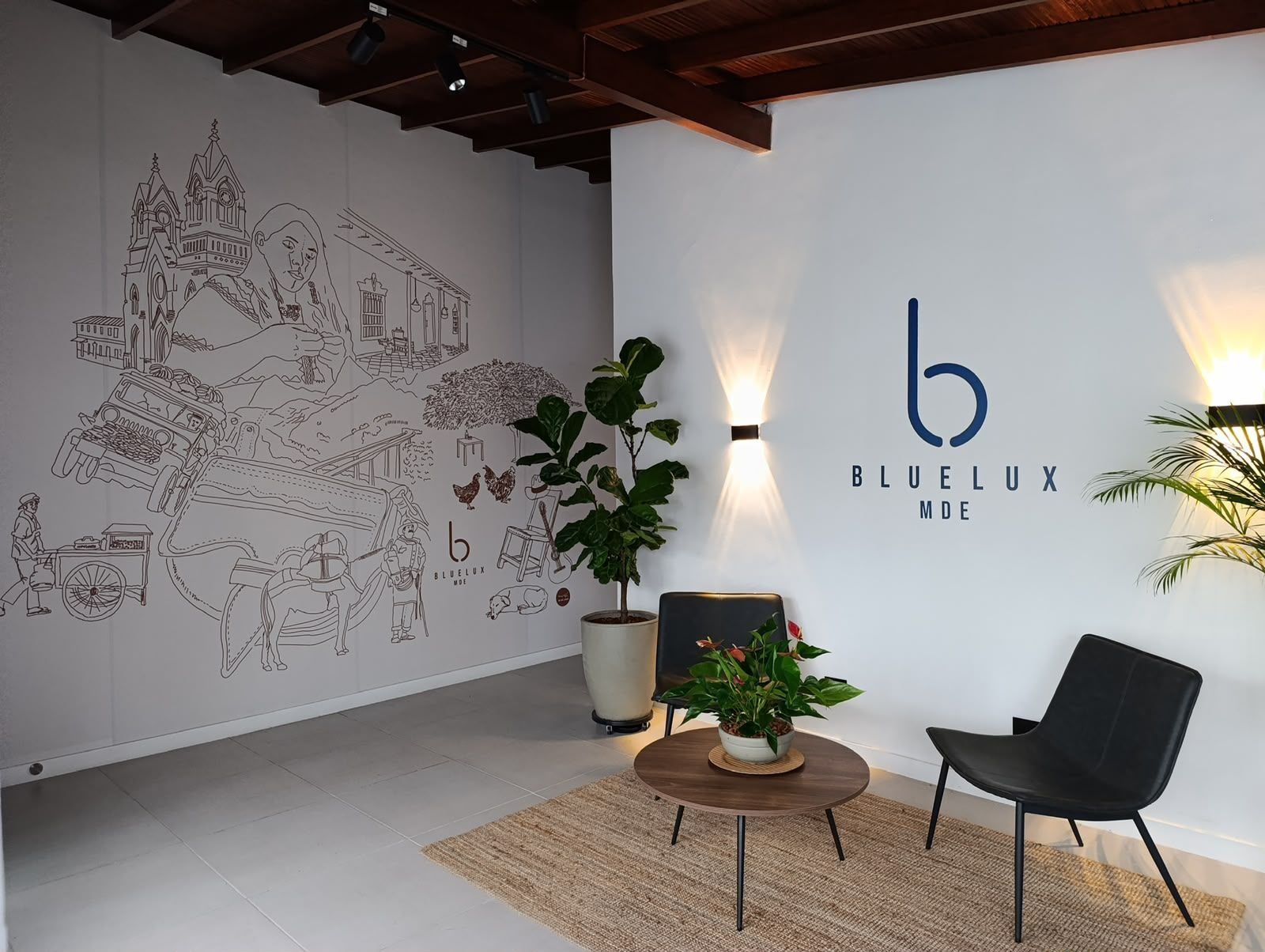 A room with a large wall mural, a round wooden table with a potted plant, a black chair, and a wall-mounted light fixture.
