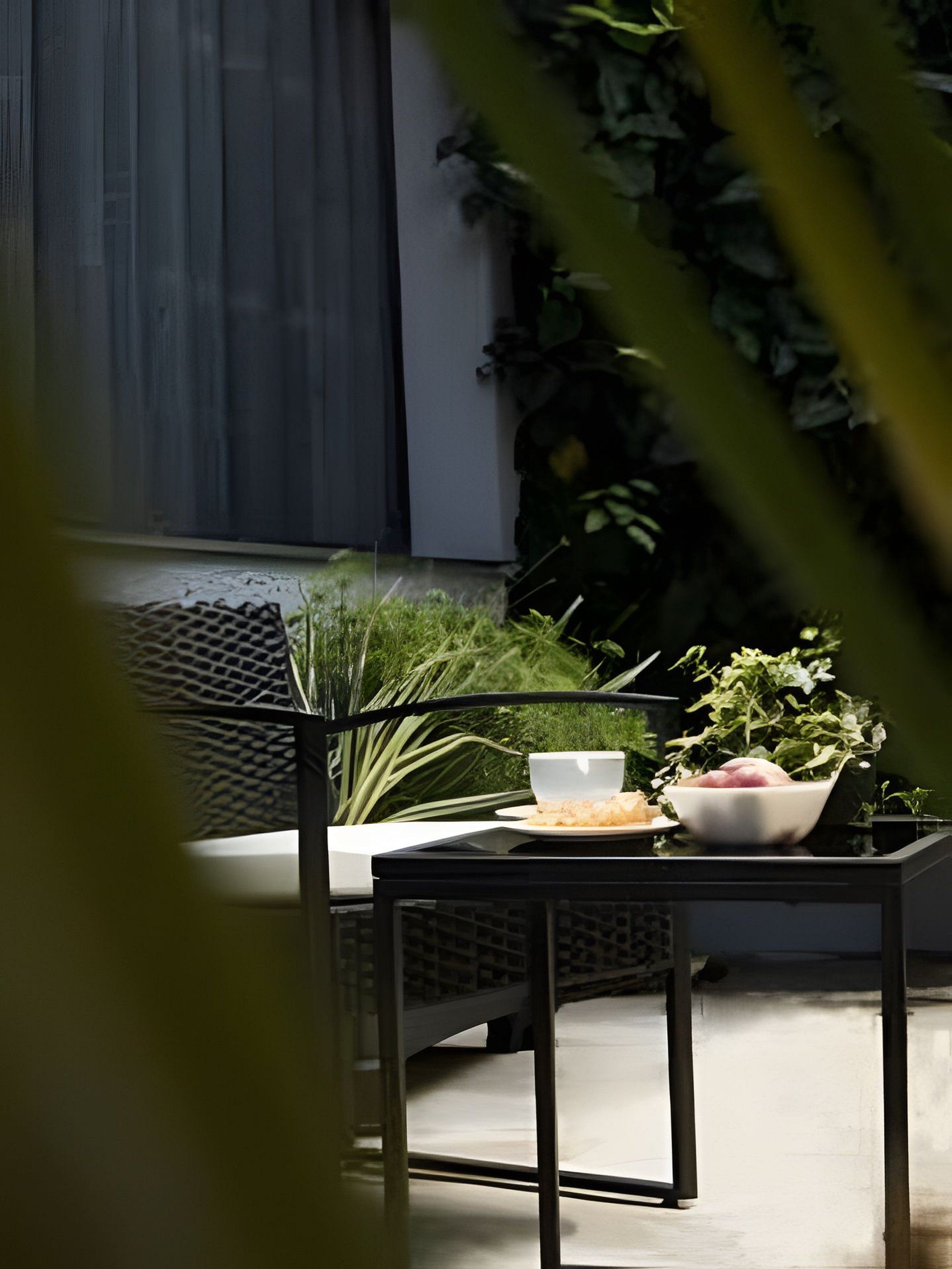 Un espace extérieur aménagé avec une table et des chaises, entouré de verdure et donnant sur une fenêtre.