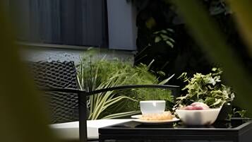 Un espace extérieur aménagé avec une table et des chaises, entouré de verdure et donnant sur une fenêtre.