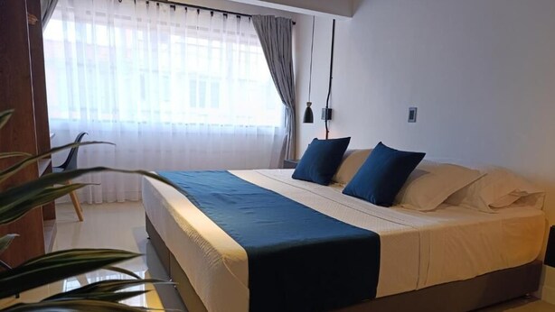 A bedroom with a bed, curtains, a plant, and a lamp. - Bluelux Med - B&B (Medellín)
