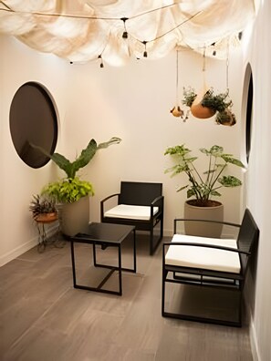 Una habitación pequeña y moderna con dos sillas negras, una mesita y varias plantas en macetas.