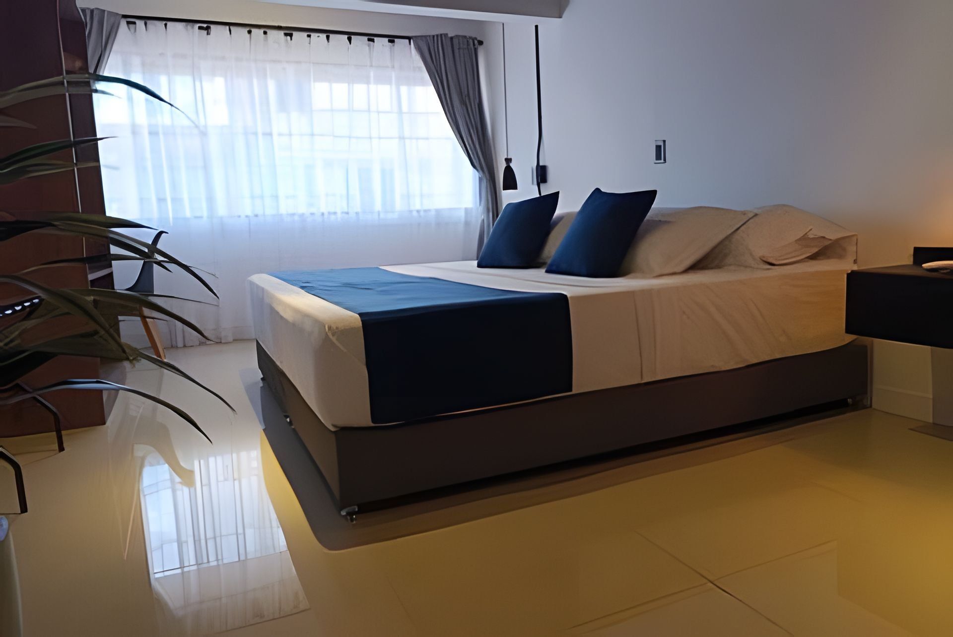 A modern bedroom with a large bed, a bedside table, a lamp, and a window with curtains.