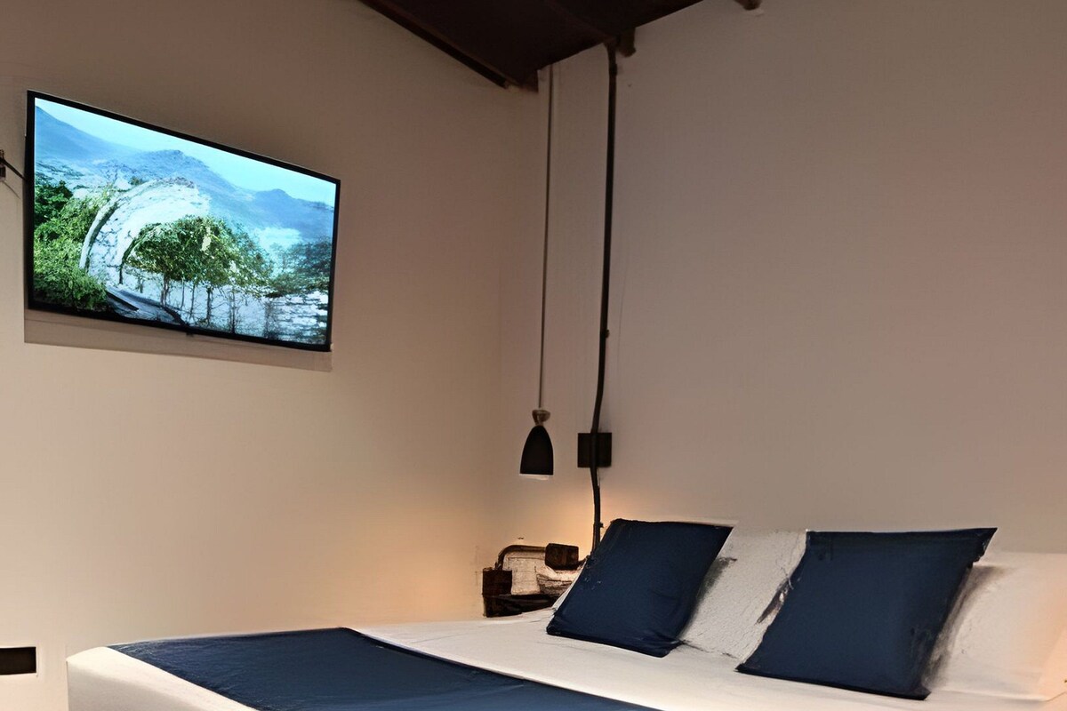 A modern bedroom with a large bed, a flat-screen TV on the wall, and a simple nightstand.