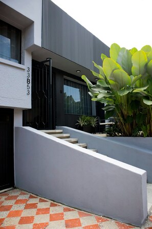 A modern building with a grey facade, a set of stairs leading to the entrance, and a large green plant in the foreground.