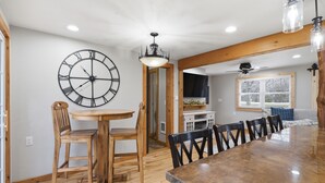 Un coin repas avec une table en bois, des chaises, une horloge murale et un ventilateur de plafond.