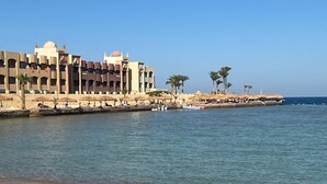 Een hotel aan de kust met uitzicht op het strand, palmbomen en een waterlichaam.