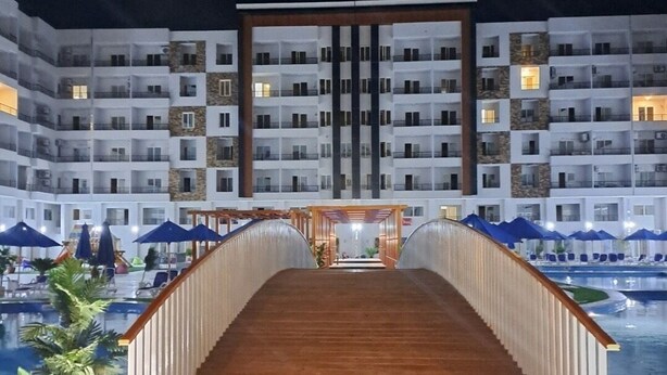 Een hotel met een zwembad, een houten brug en een meerlaags gebouw met balkons.