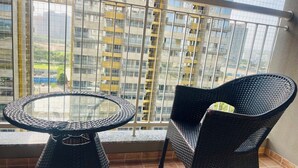 En balkon med et glasbord og fletstole, med udsigt over et bybillede med høje bygninger.