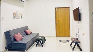 En moderne stue med sofa, loftventilator, klimaanlæg, en trædør og et tv ophængt på væggen.