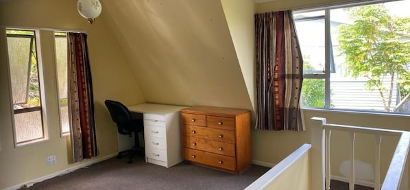 Ein Schlafzimmer mit Schreibtisch, Kommode und einem fenster mit Vorhängen.