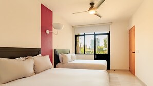 Ein Hotelzimmer mit zwei Betten, einem Deckenventilator, einem Fenster mit Blick auf Gebäude und einer roten Akzentwand.