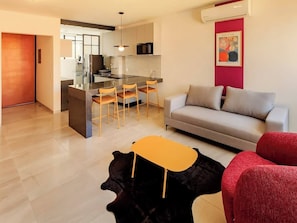 Una sala de estar moderna con un sofá, un comedor con sillas, una mesita y una cocina al fondo.