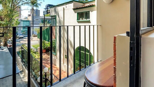 Ein Balkon mit Blick auf eine Straße, ein grünes Tor und ein Gebäude mit einem Ziegeldach.