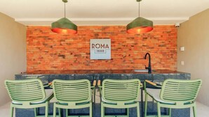 Eine Küche mit Backsteinwand, einem Schild mit der Aufschrift 'ROMA 1888' und vier grünen Stühlen.