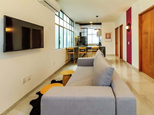 Un salon moderne comprenant un canapé, un téléviseur et un coin repas avec des chaises et une table.