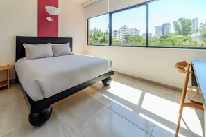 Une chambre moderne avec un lit, un bureau et une grande fenêtre donnant sur la ville.